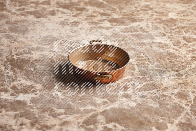 A small copper pan on beige marble background