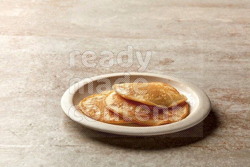 Three stacked plain pancakes in a beige plate on grey beige background