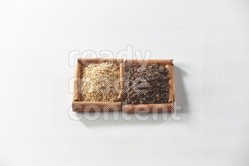 مربعان من أعواد القرفة ممتلئان بالقرنفل وبذور السمسم علي خلفية بيضاء