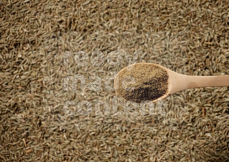 A wooden spoon full of cumin powder on a cumin seeds background