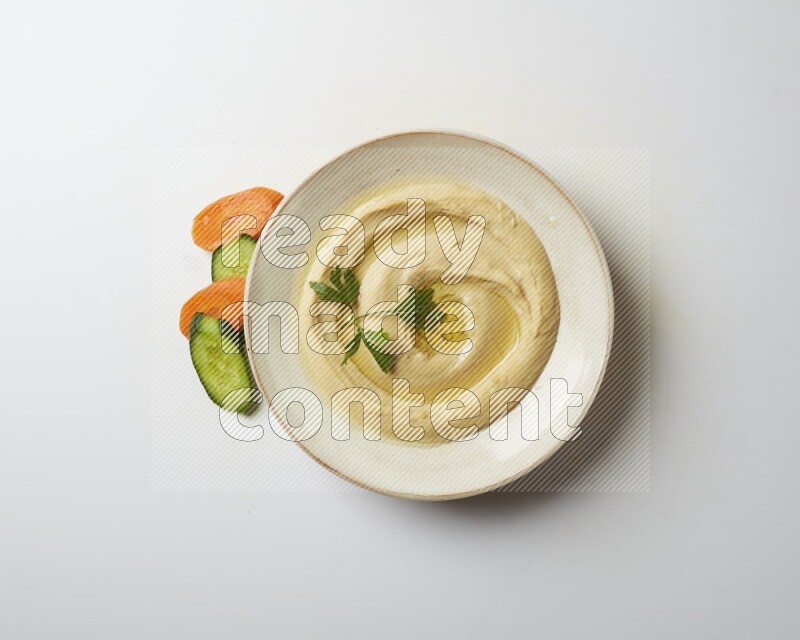 Hummus in a pottry plate garnished with parsley on a white back ground