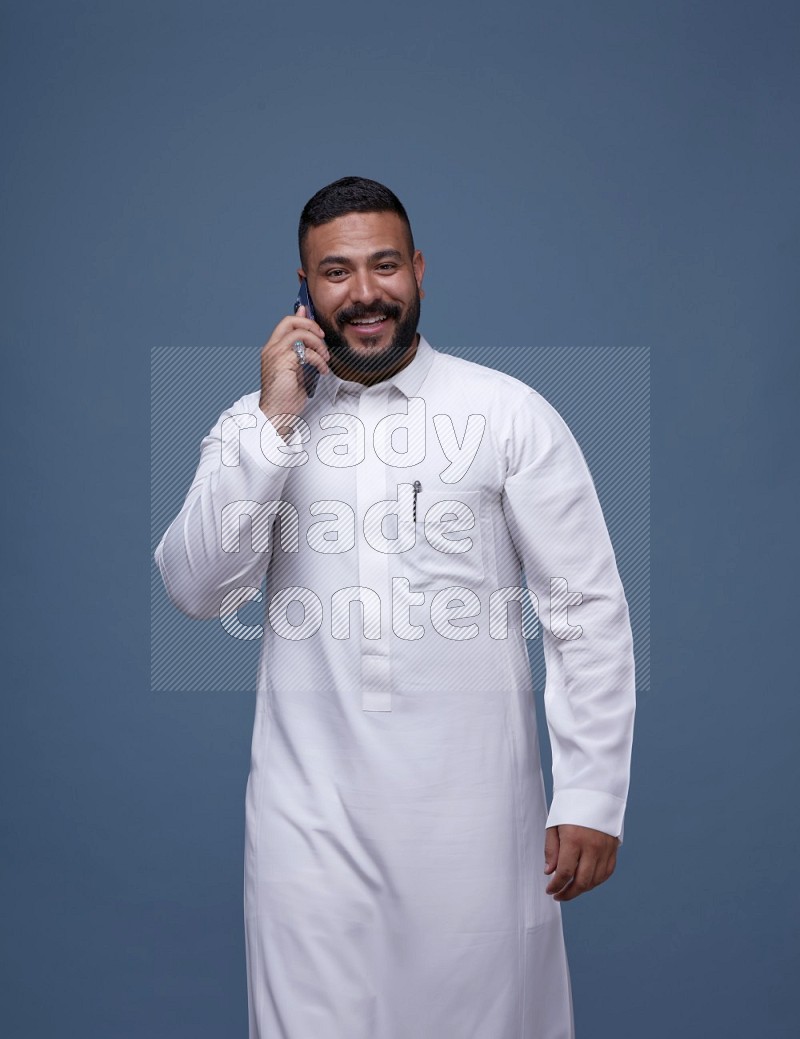 A Saudi man calling on blue background wearing Saudi Thob