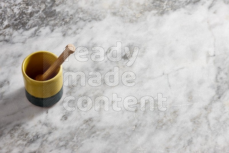 Multicolored Pottery Cup with wooden honey handle in it, on grey marble flooring, 65 degree angle