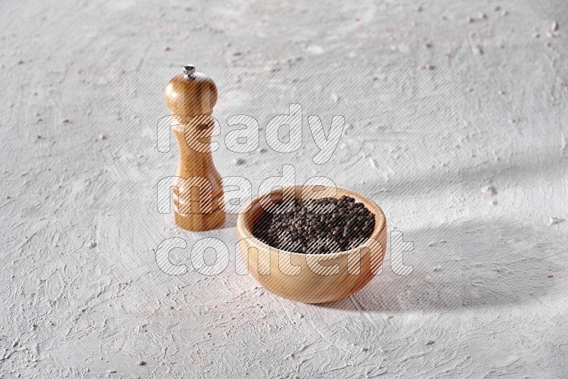 حبات الفلفل الأسود في وعاء خشبي مع مطحنة خشبية علي خلفية بيضاء