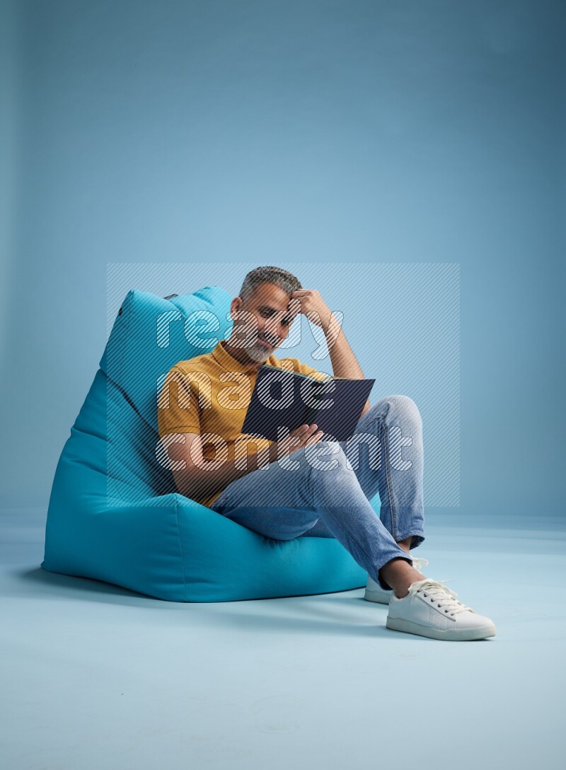 A man sitting on a blue beanbag and reading a book