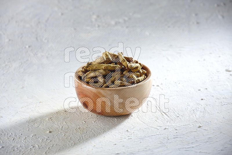 A wooden bowl full of dried turmeric whole fingers on a textured white flooring
