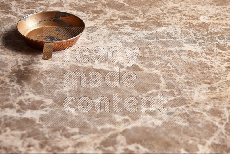 A small copper pan on beige marble background