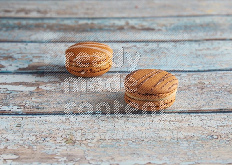 45º Shot of of two assorted Brown Irish Cream, and light brown Almond Cream macarons next to each other on light blue background