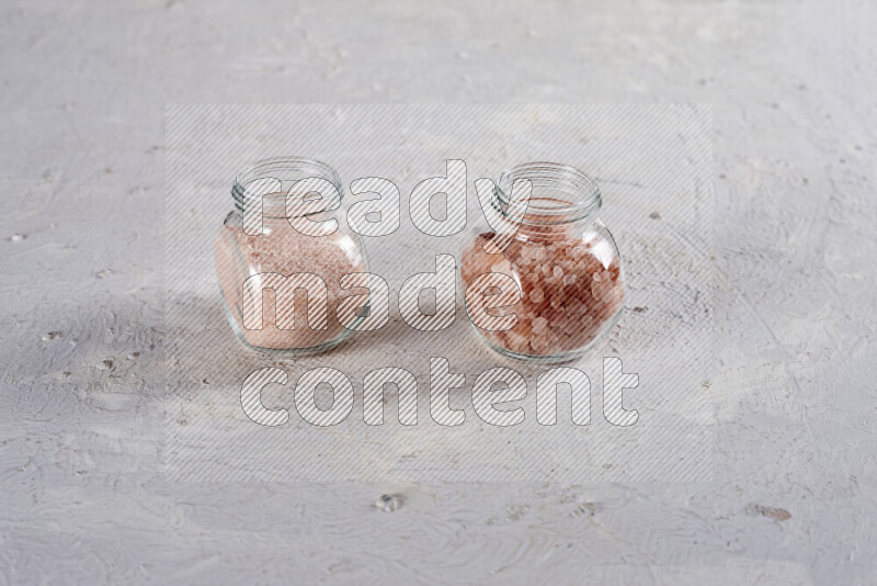 2 glass jars one is filled with fine himalayan salt and the other with coarse himalayan salt on white background