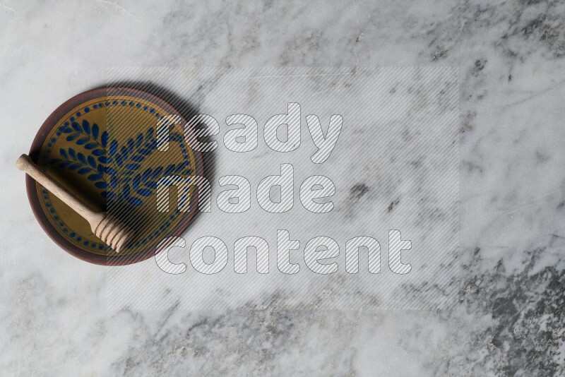 Decorative pottery plate with wooden honey dipper in it on grey marble background