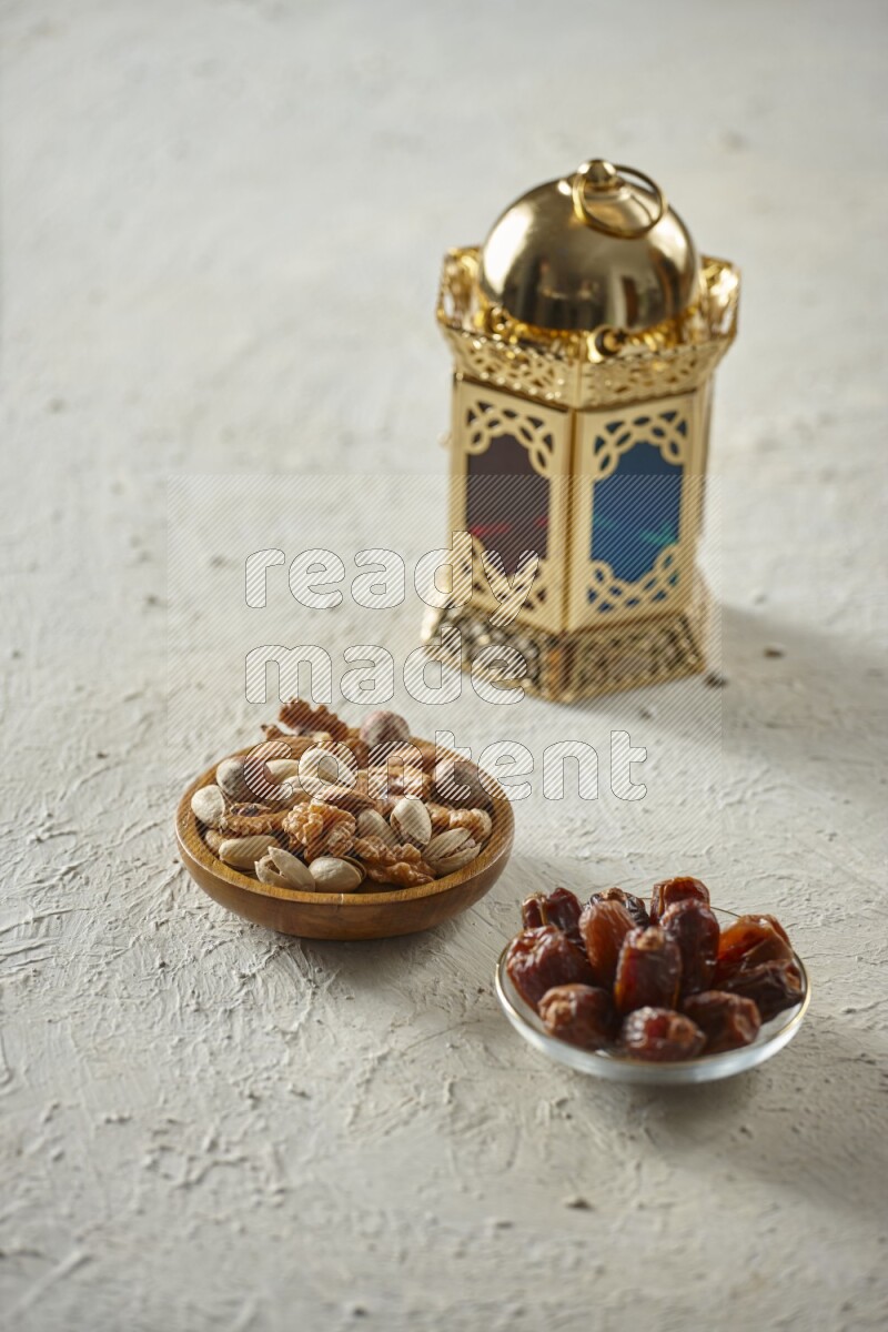 A golden lantern with different drinks, dates, nuts, prayer beads and quran on textured white background