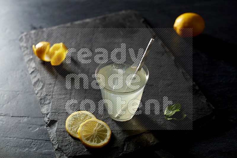 A glass of lemon juice with a straw on black background