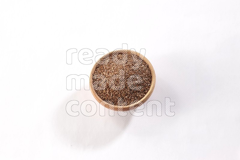 A wooden bowl full of flax seeds on a white flooring