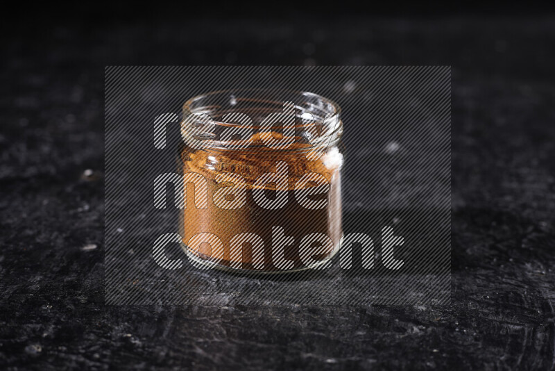 A glass jar full of ground paprika powder on black background