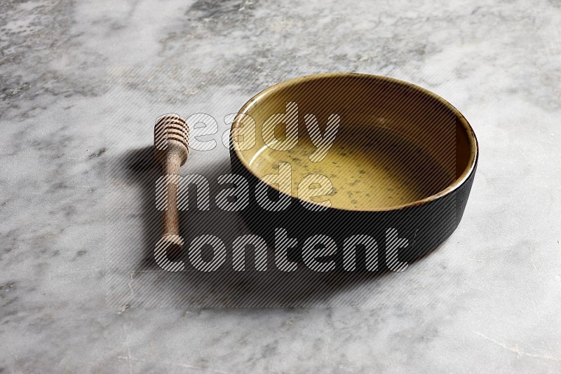Multicolored Pottery oven plate with wooden honey handle on the side with grey marble flooring, 45 degree angle