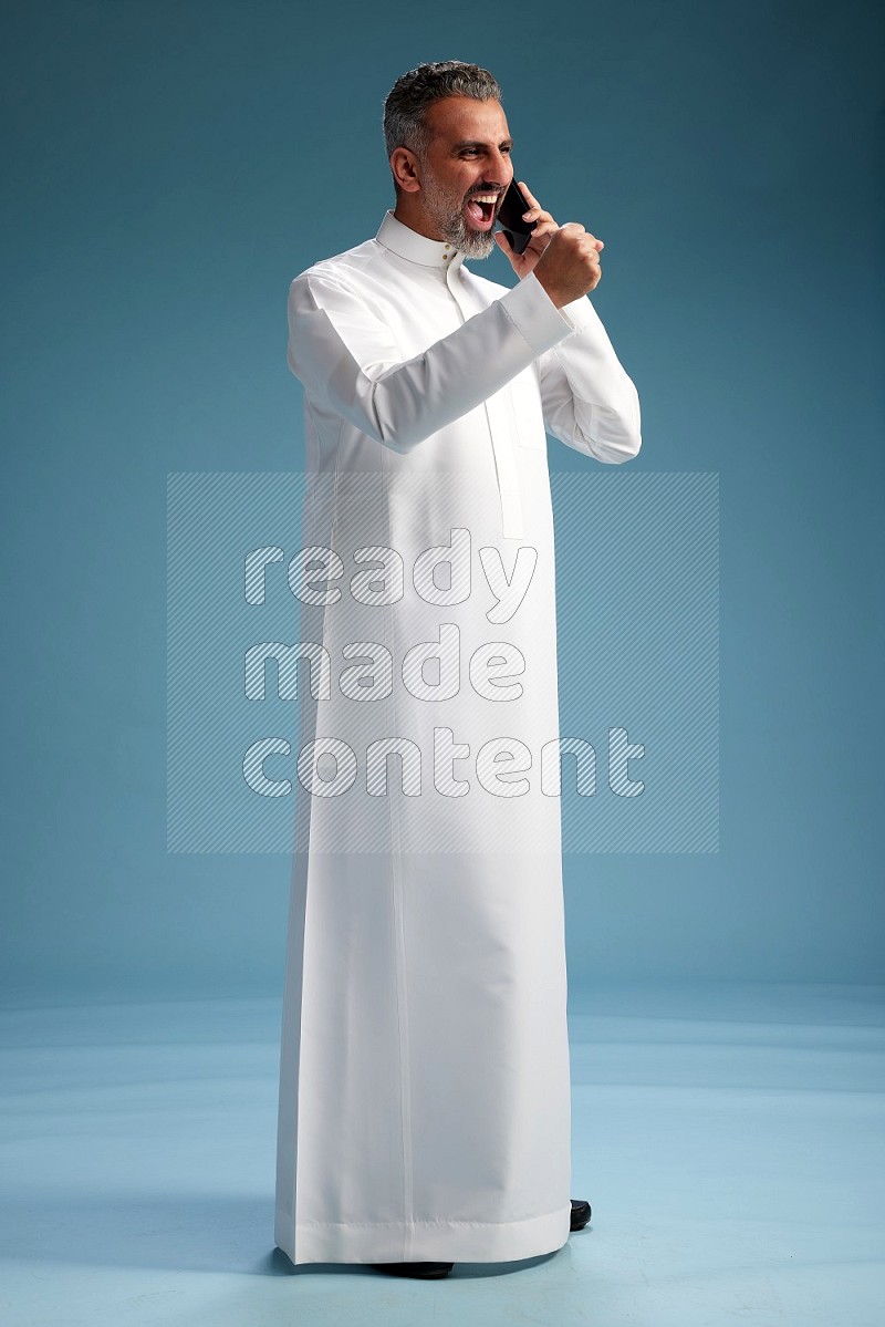Saudi man wearing thob talking on the phone on blue background