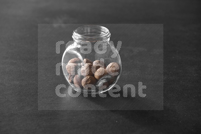 A glass spice jar full of nutmeg on black flooring