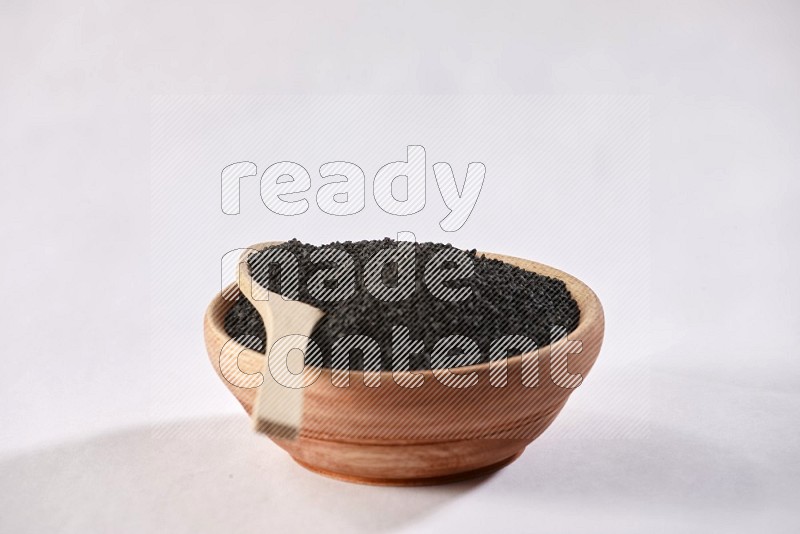 A wooden bowl and wooden spoon full of black seeds on a white flooring