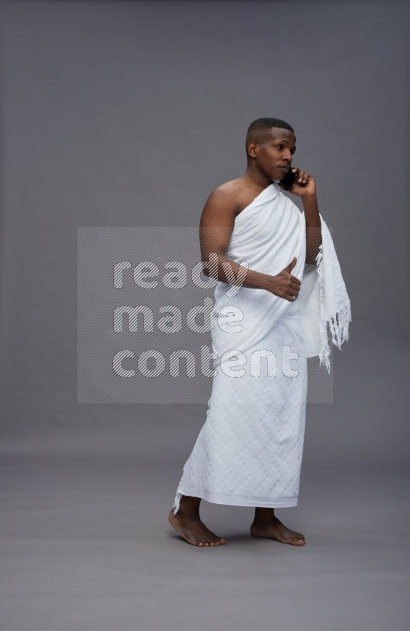 A man wearing Ehram Standing talking on phone on gray background
