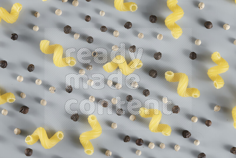 Raw pasta with different ingredients such as cherry tomatoes, garlic, onions, red chilis, black pepper, white pepper, bay laurel leaves, rosemary, cardamom and mushrooms on light blue background