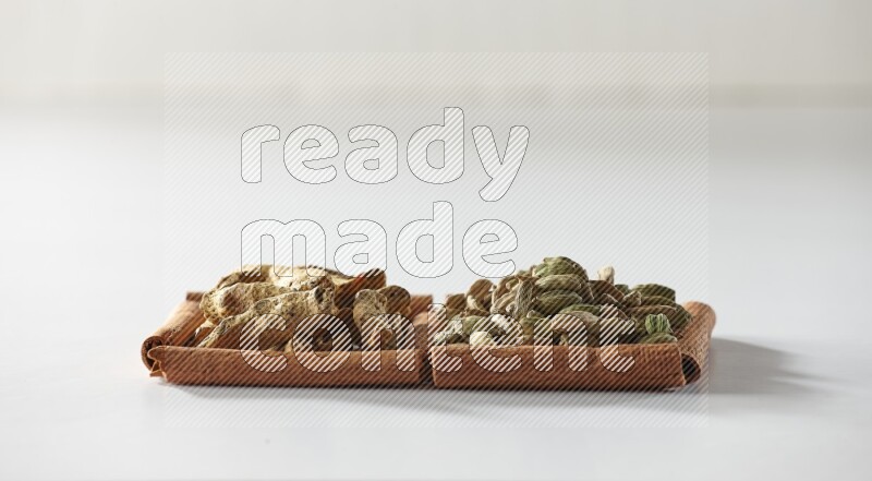 مربعان من أعواد القرفة ممتلئان بحبوب الهيل وأصابع الكركم علي خلفية بيضاء