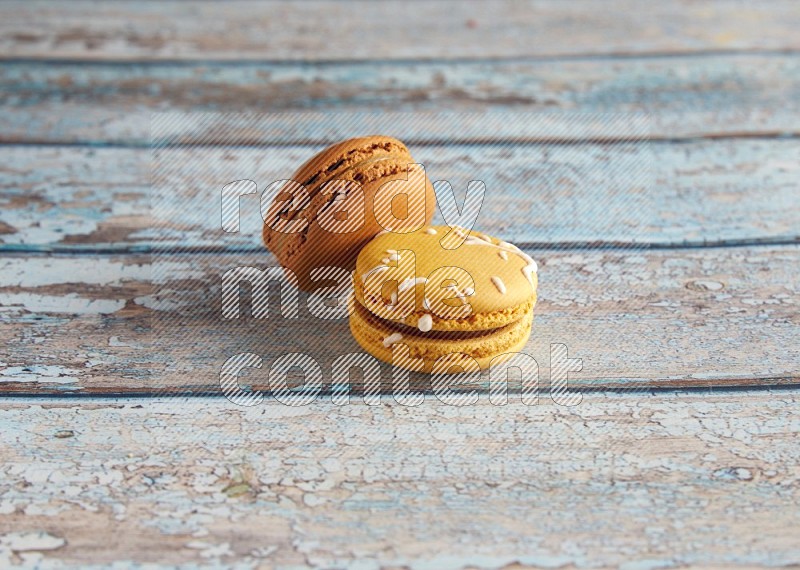 45º Shot of of two assorted Brown Irish Cream, and Yellow Piña Colada macarons on light blue background