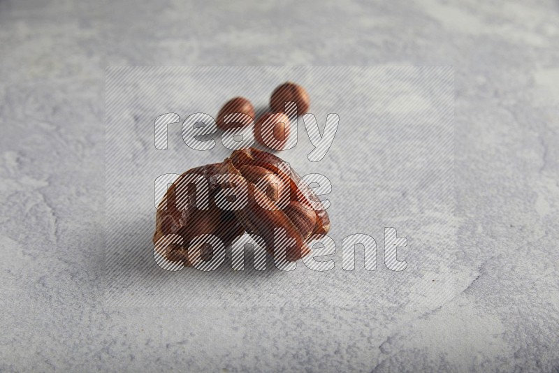Two hazulnut stuffed dates with unroasted hazelnuts on light grey background