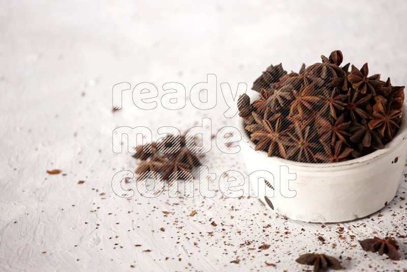 Star Anise in a white bowl and more of it sprinkled on white background