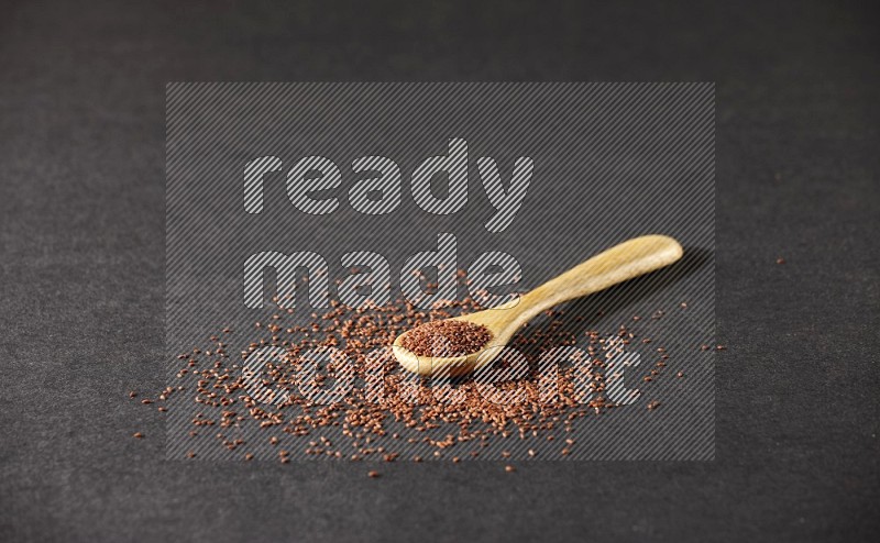 A wooden spoon full of garden cress seeds and seeds spread beside it on a black flooring
