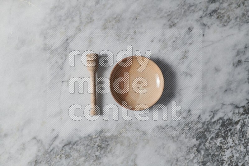 Multicolored pottery plate with wooden honey dipper on the side on grey marble background