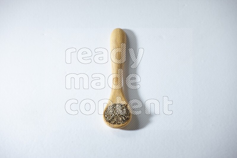 A wooden spoon full of cumin seeds on a white flooring
