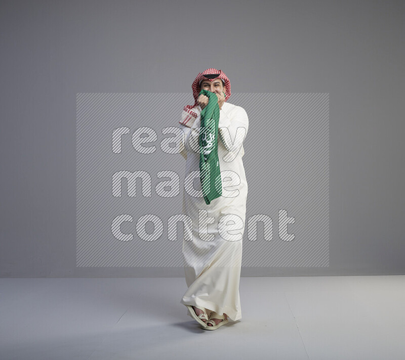 رجل سعودي يرتدي ثوب ابيض وشماغ احمر يقبل علم السعودية