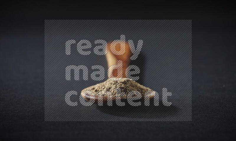 A wooden ladle full of cardamom powder on black flooring