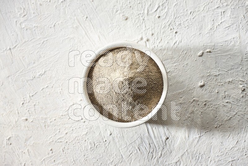 white pottery bowl full of white pepper powder on textured white flooring
