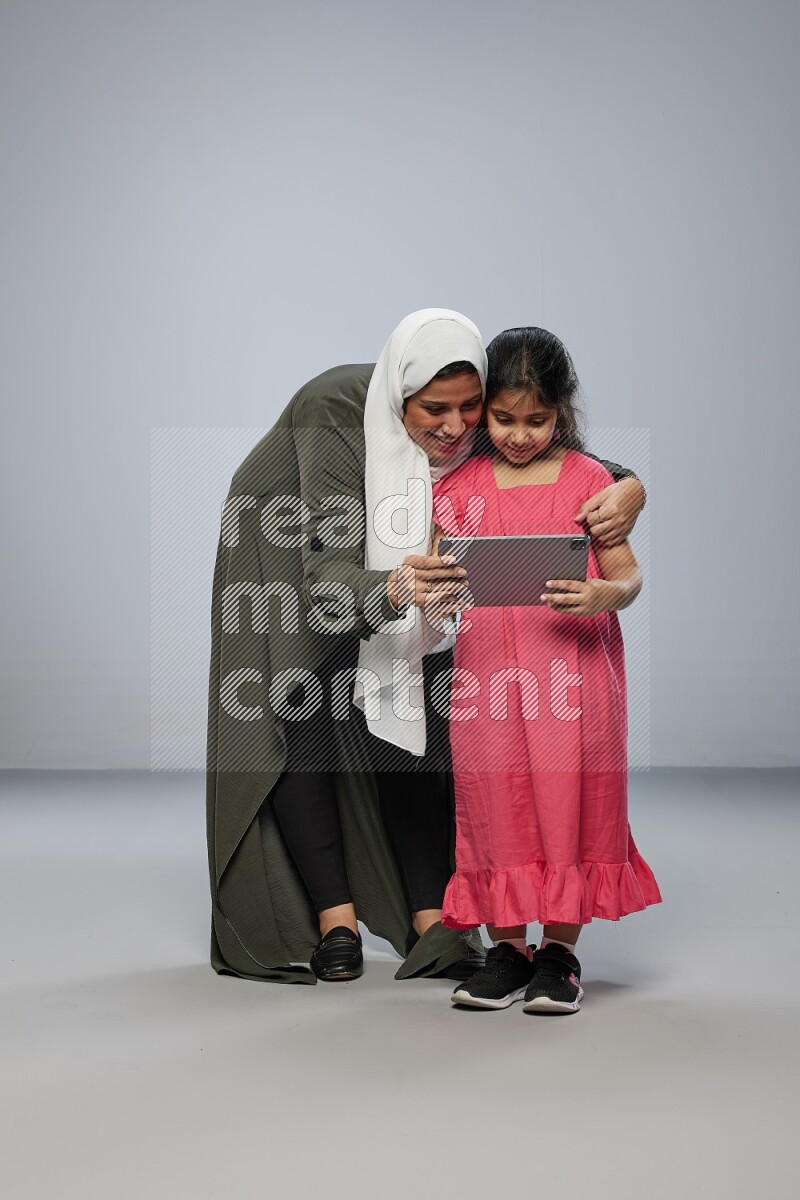 A girl holding an Ipad with her mother on gray background