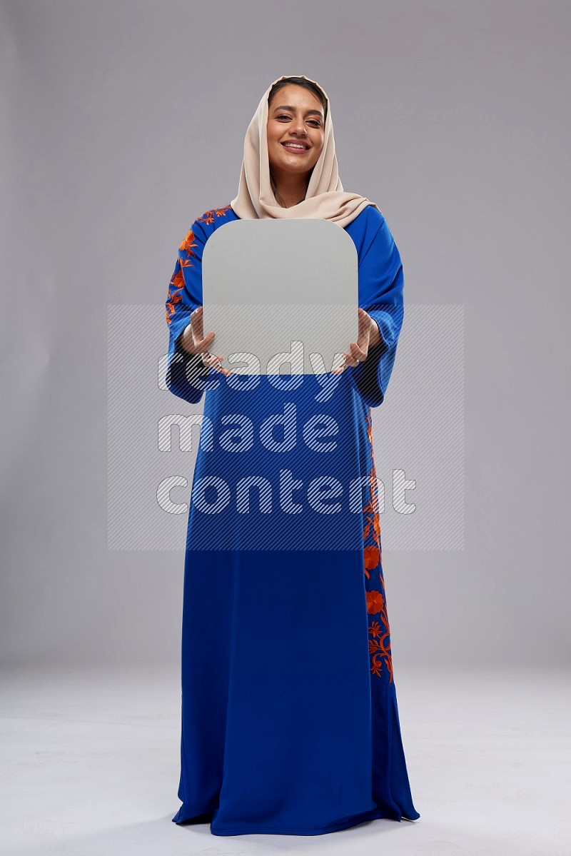 A Saudi woman standing wearing Jalabeya holding a social media sign