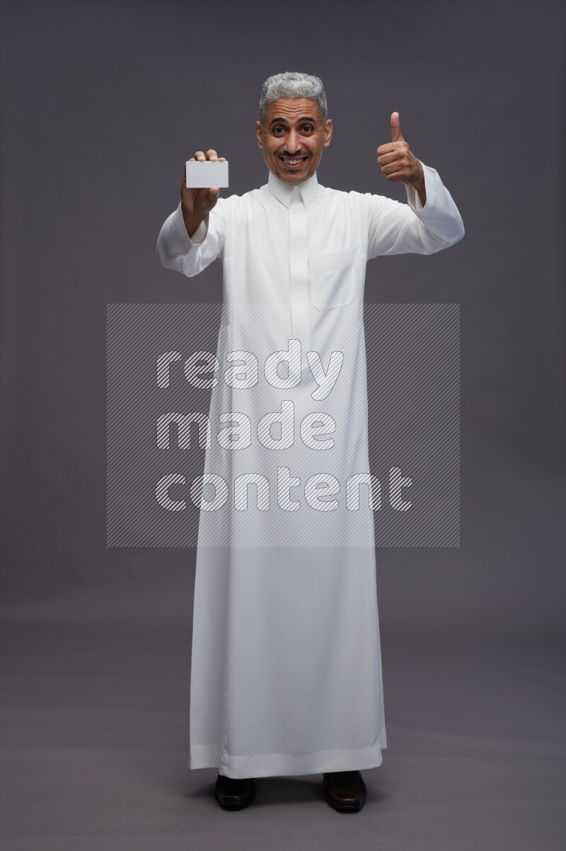 Saudi man wearing thob standing holding ATM card on gray background