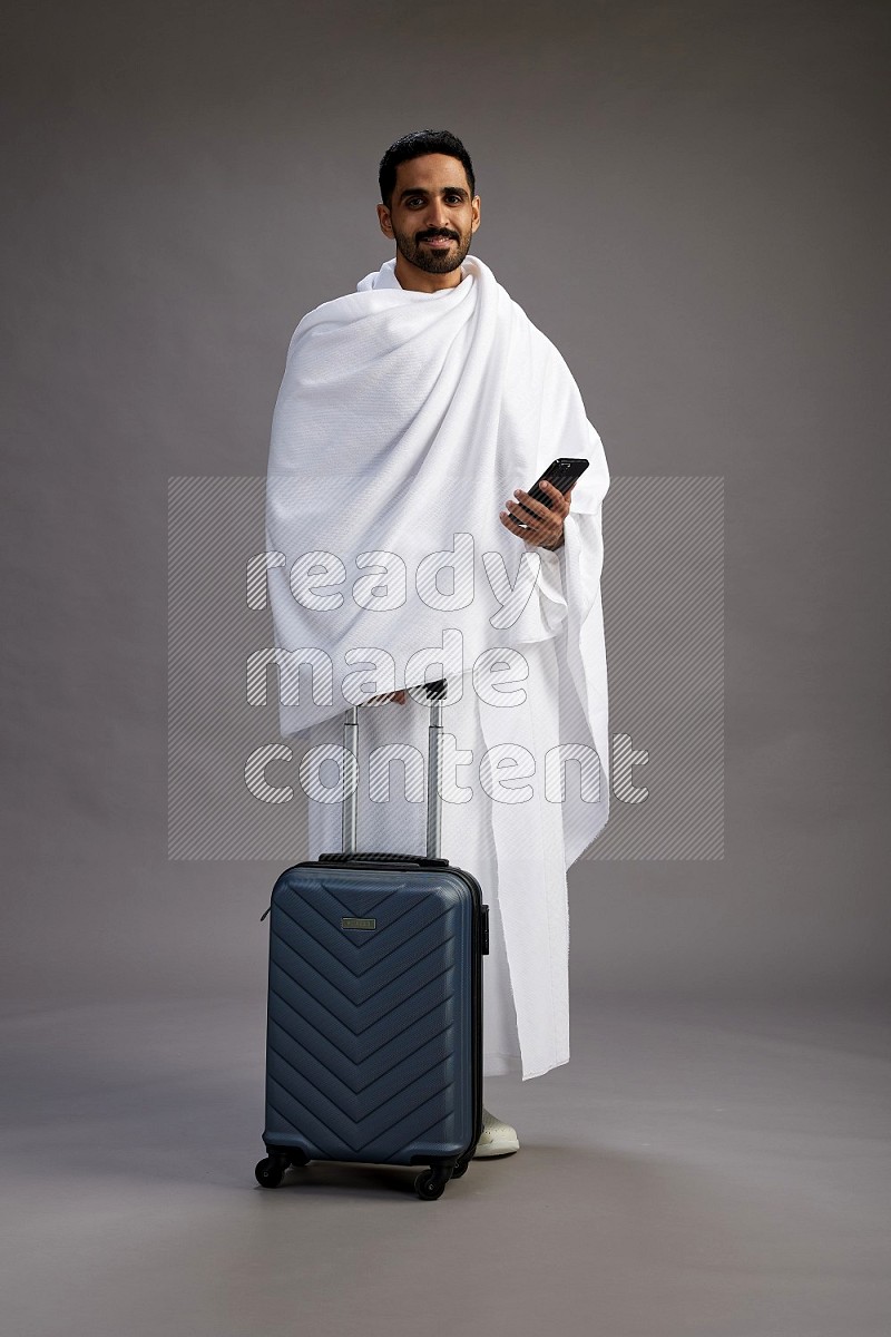 A man wearing Ehram Standing holding traveling bag on gray background