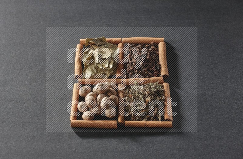 4 squares of cinnamon sticks full of bay laurel leaves, dried basil, cloves and nutmegs on black flooring