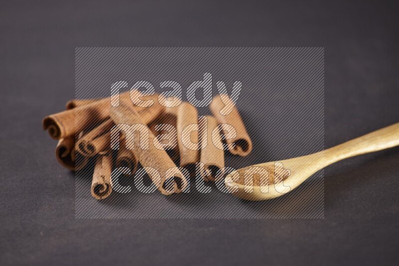 Cinnamon sticks stacked beside a wooden spoon full of cinnamon powder on black background
