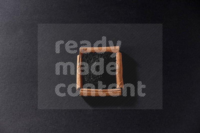 A single square of cinnamon sticks full of black seeds on black flooring
