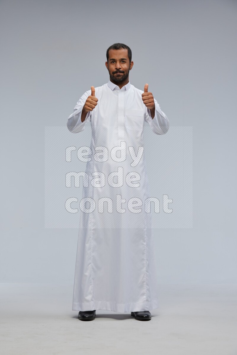 Saudi man Wearing Thob standing interacting with the camera on Gray background