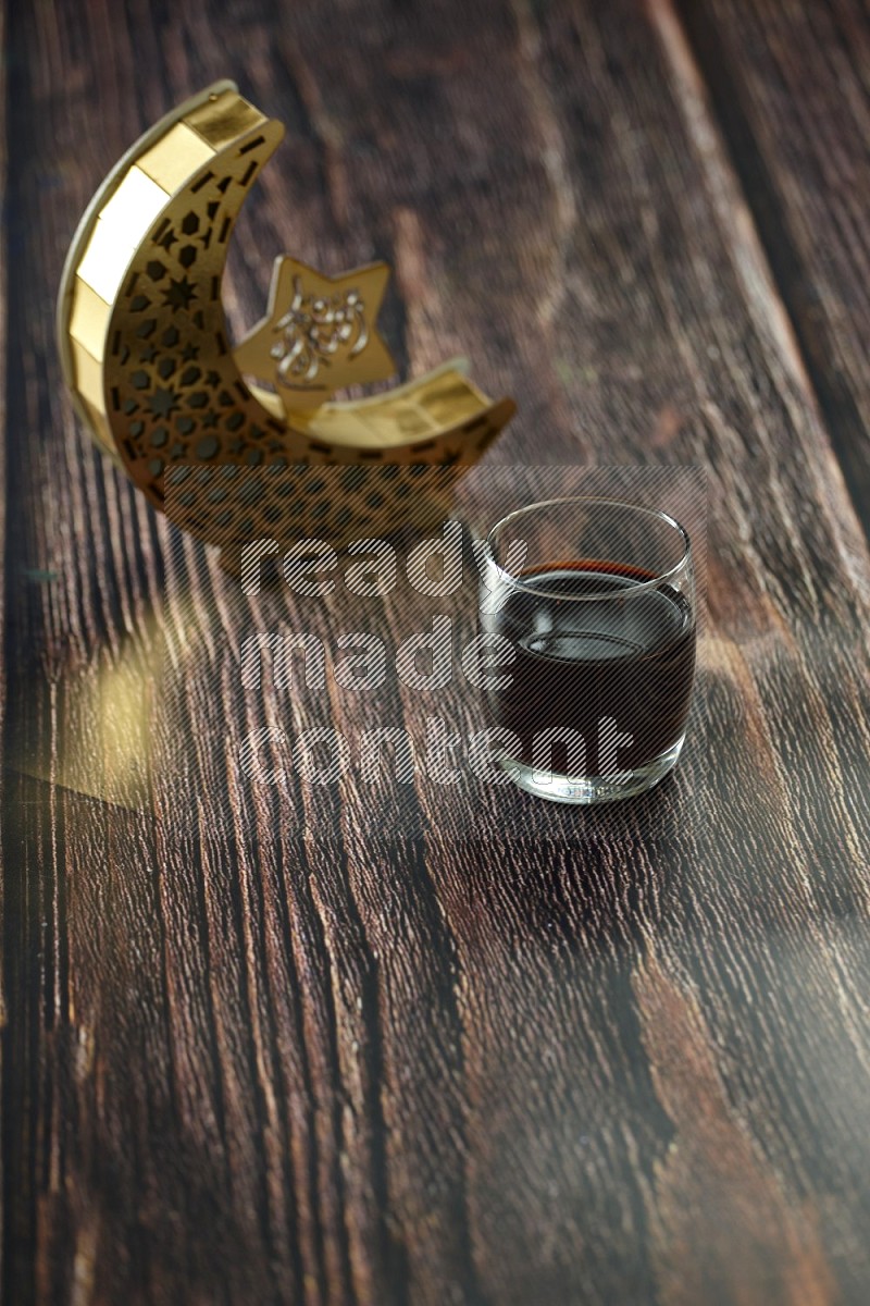 A wooden golden crescent lantern with different drinks, dates, nuts, prayer beads and quran on brown wooden background