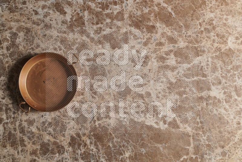 A small copper pan on beige marble background