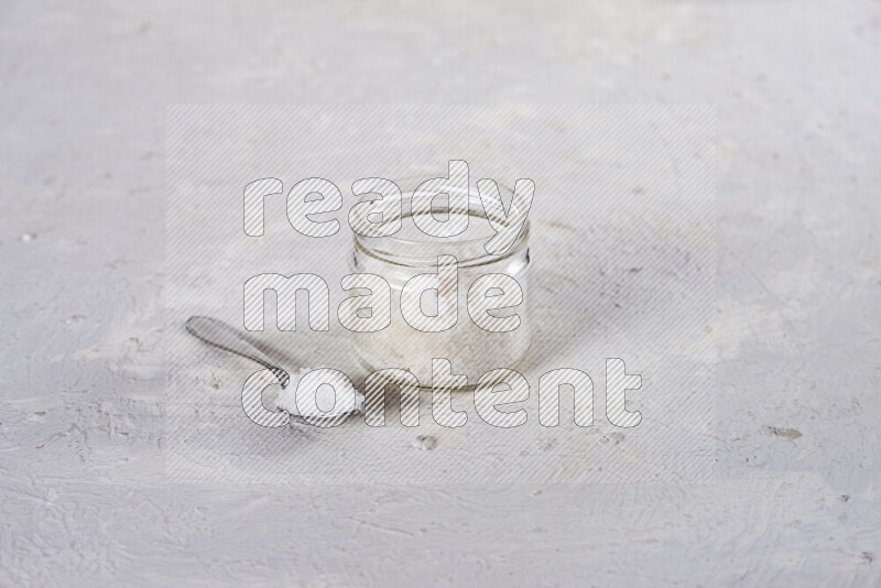 A glass jar full of coarse sea salt crystals on white background