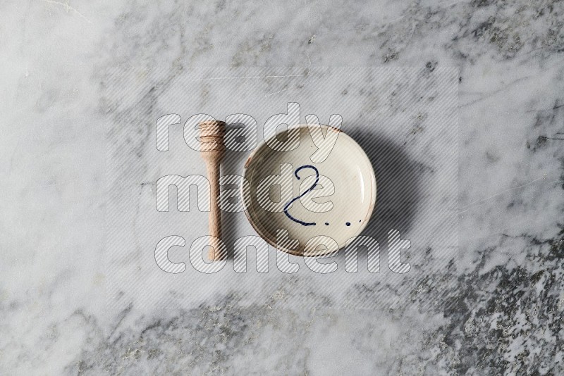 Multicolored Pottery Bowl with wooden honey handle on the side on grey marble flooring, Top view