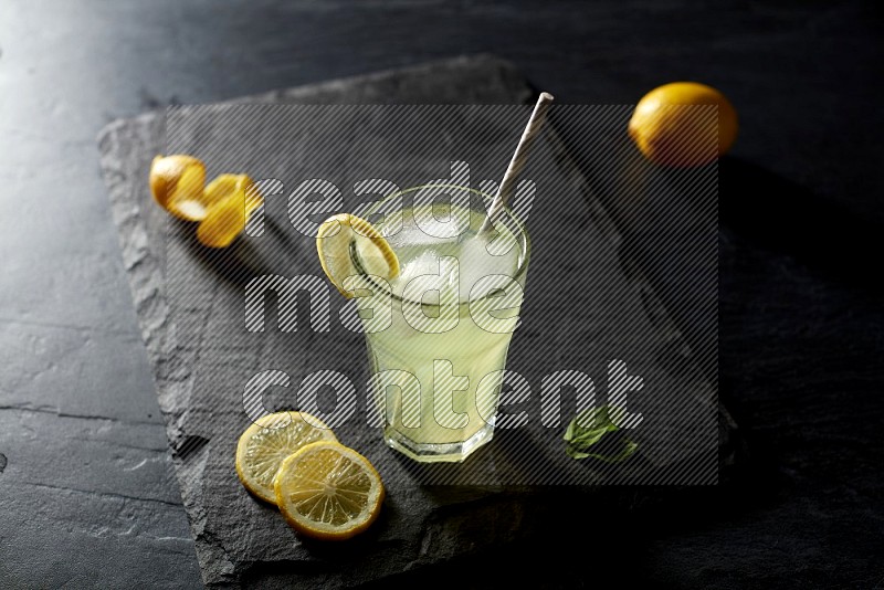 A glass of lemon juice with a straw on black background