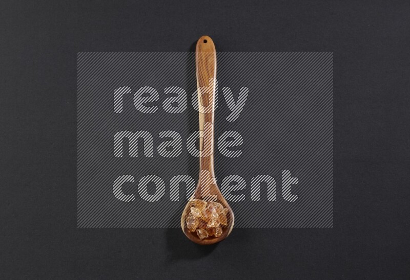 A wooden ladle filled with gum arabic on black flooring