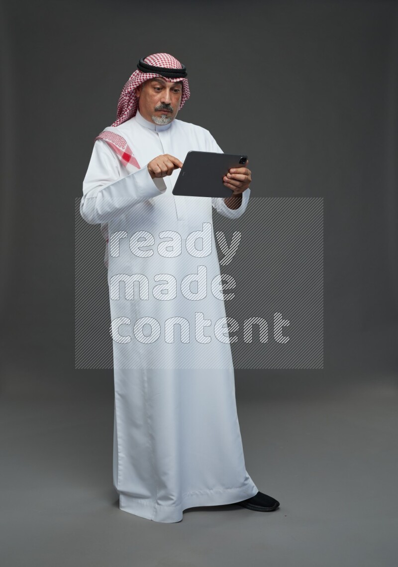 Saudi man with shomag Standing working on tablet on gray background