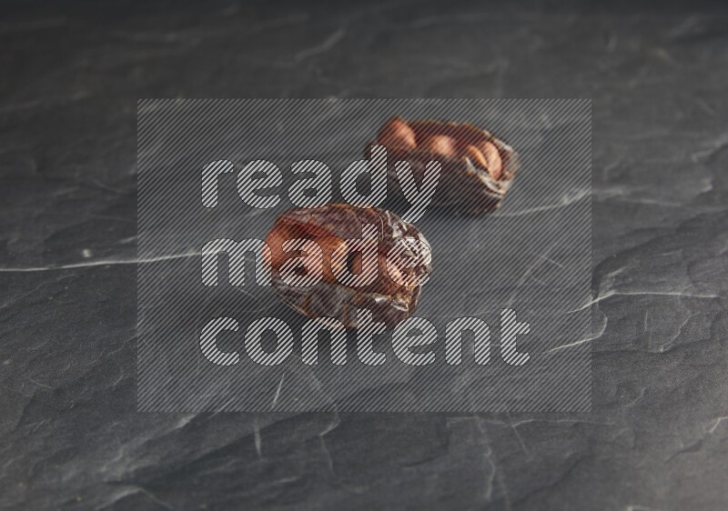 two hazelnuts stuffed madjoul dates on a black textured background